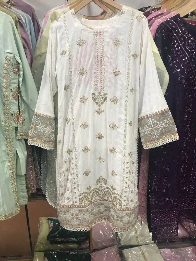 An off-white embroidered kurta with gold and beige detailing, hanging on a wooden hanger in a clothing store.