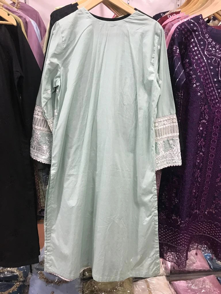 A sage green long tunic dress with white lace cuffs hanging on a wooden hanger in a clothing store.