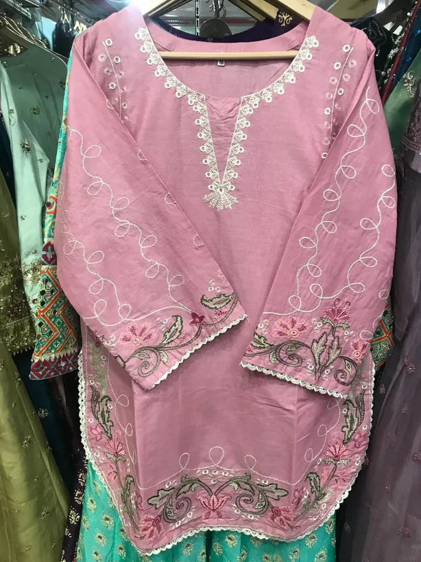 A pink embroidered kurta with white floral embroidery and mirror work, displayed on a hanger in a clothing store.